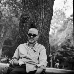 Mann lehnt lässig am Baum und fasst sich an den Bauch